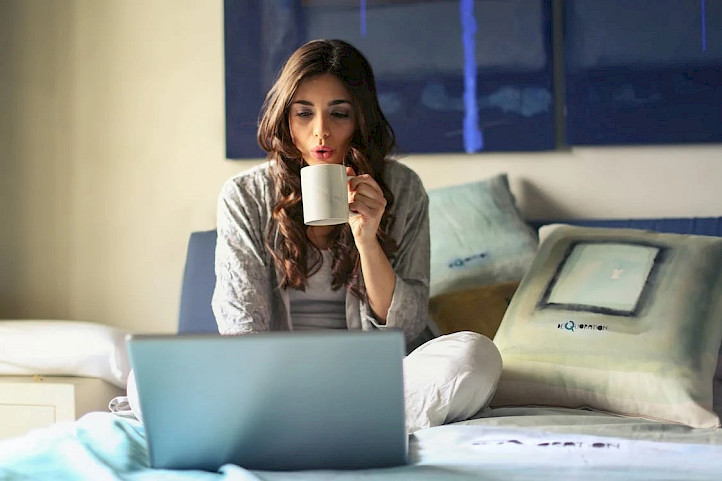 Woman drinking coffee and looking at a laptop.