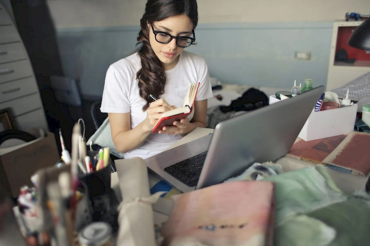 Woman taking notes looking at a laptop screen.